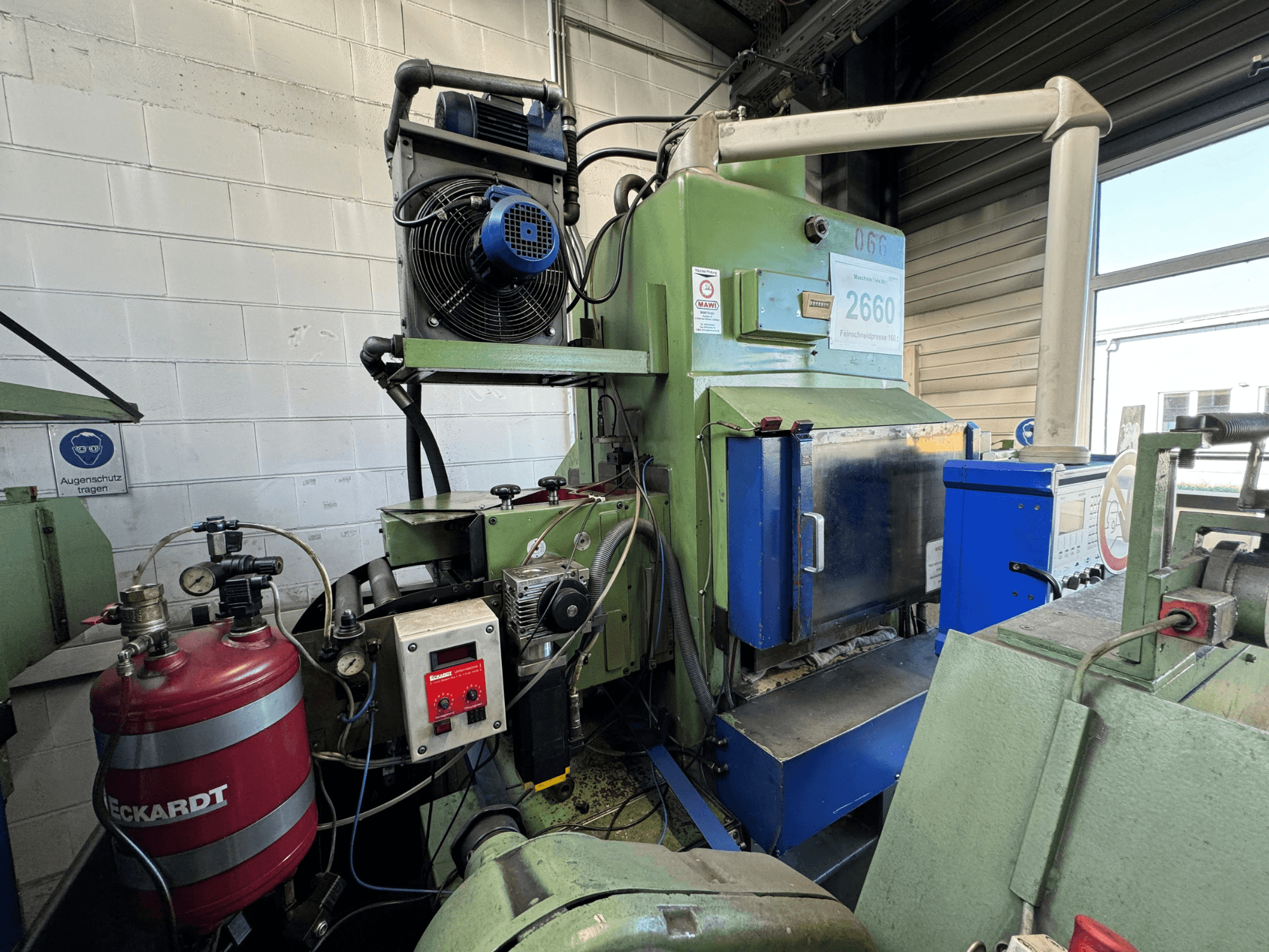 Industriële machine met ventilator, bedieningspaneel en rode brandstoftank; gezien vanaf de voorkant in een werkplaats.