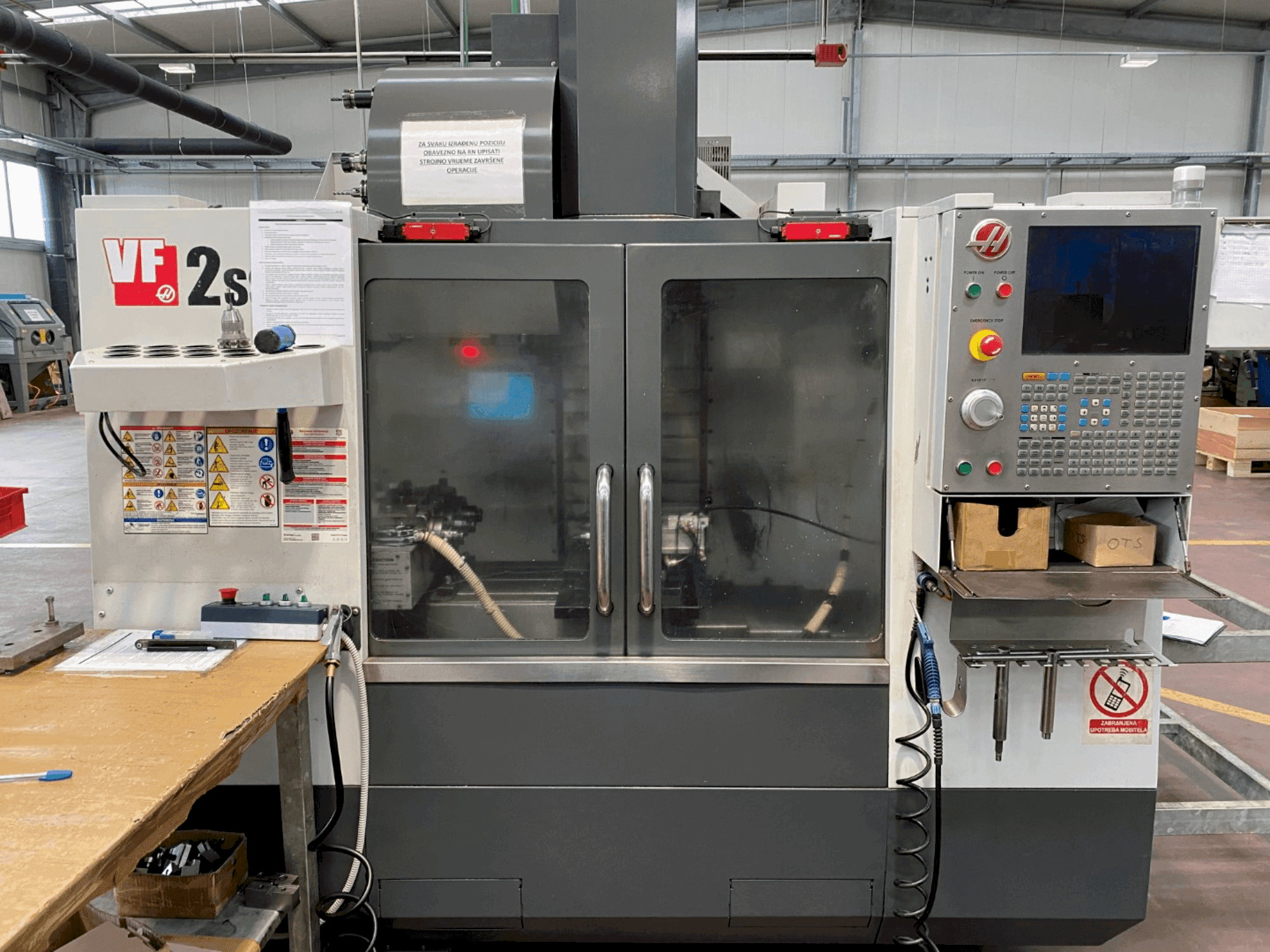 Haas VF-2SS bewerkingscentrum in vooraanzicht, met bedieningspaneel, koelvloeistofslang en veiligheidslabels aan de zijkant.