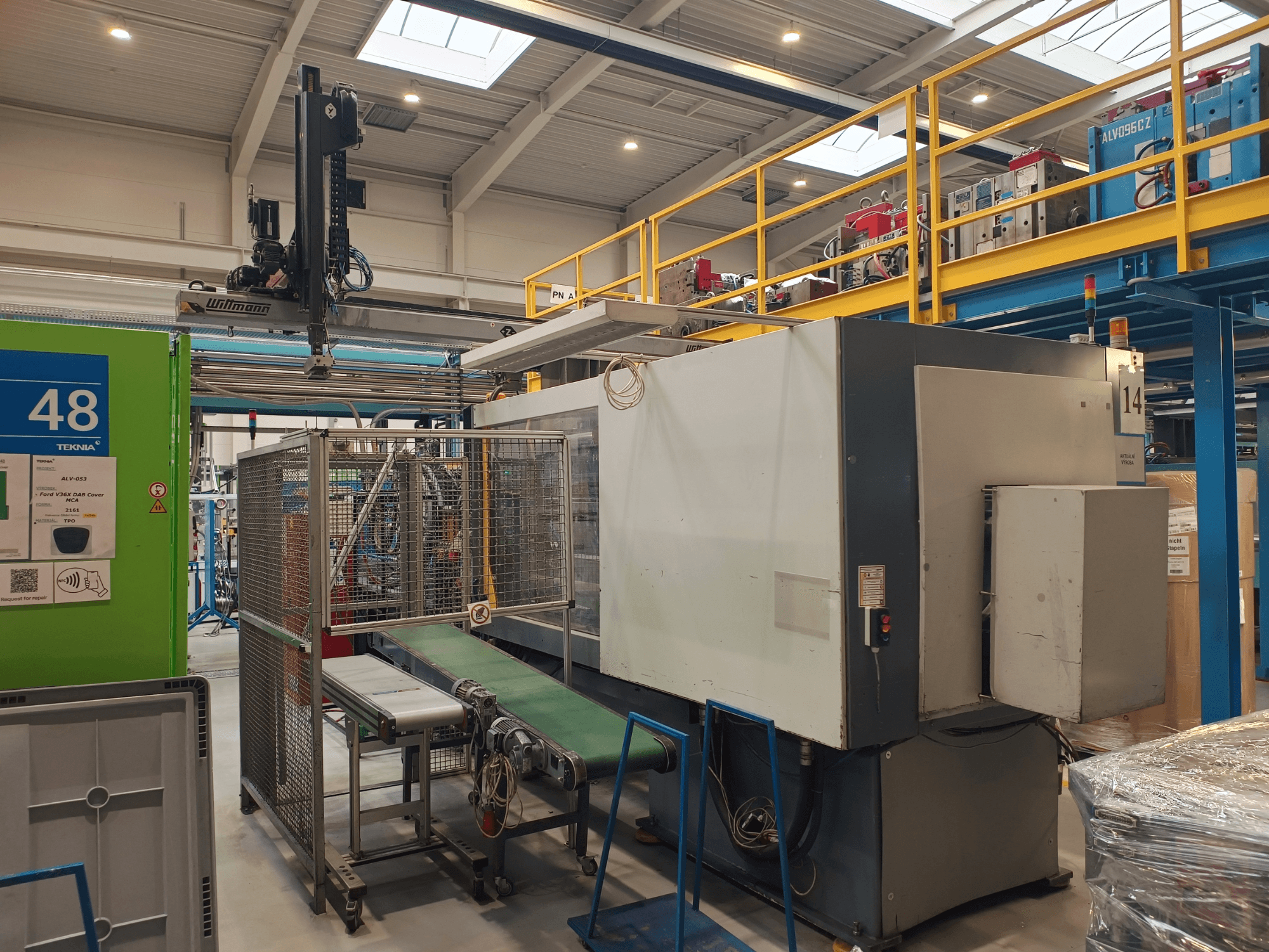 Industriële automatiseringsapparatuur met groene transportband met het label '48' en een bovenloopkraan; zijaanzicht van de machine op de fabrieksvloer.